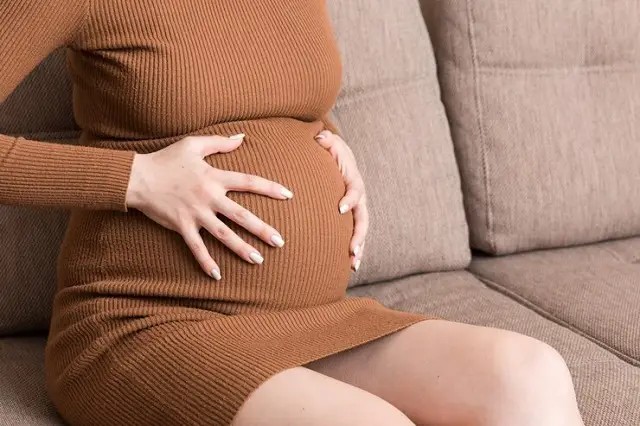 femme enceinte ayant massé le bas du ventre assis sur un canapé