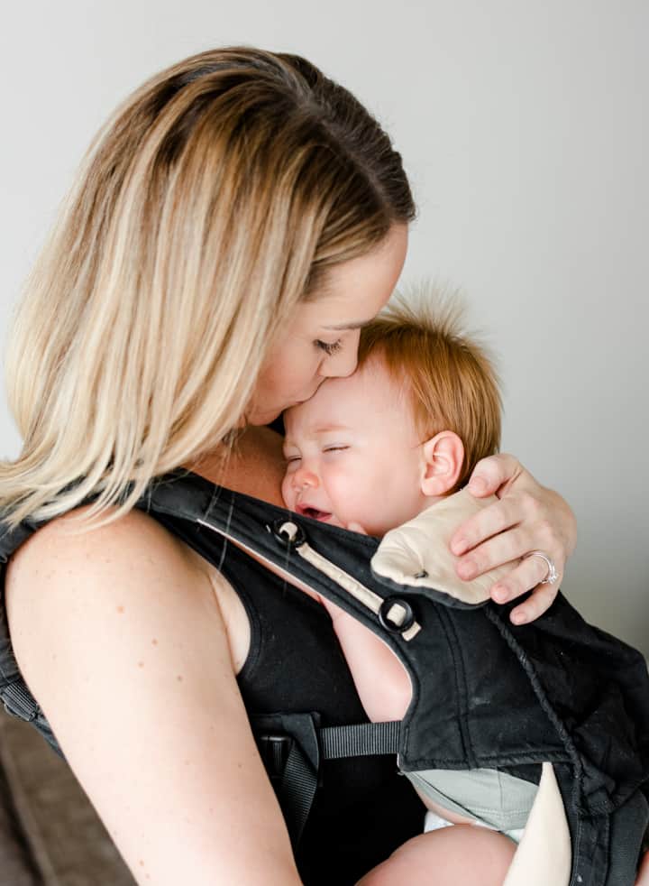 Woman carries a sleepy baby in a carrier - what is attachment parenting and its effect on brain development
