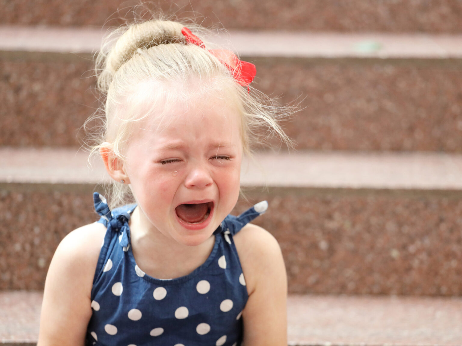 La première raison pour laquelle les parents ont du mal à calmer leurs tout-petits pendant les crises de colère, d’après les dernières recherches. little-girl-blue-dress-sits-steps-cries
