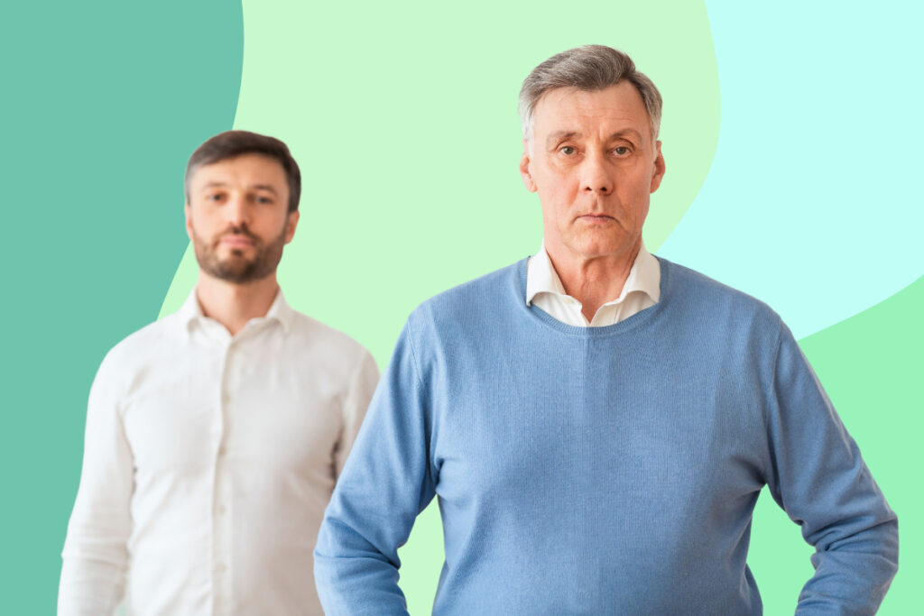 A father stands in front of his adult son, who is blurred in the background.