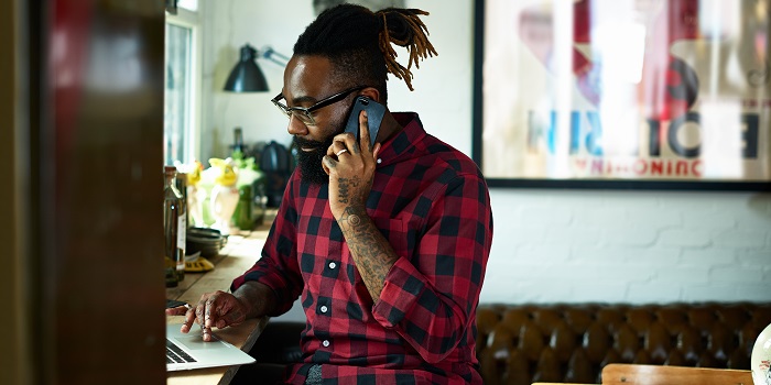 man with a checked shirt on a phone and laptop