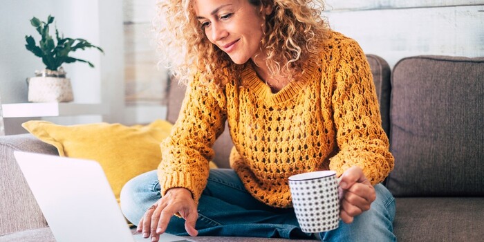 person seated on the sofa with a laptop and a cup in hand