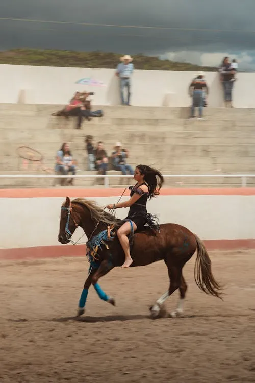 A skilled female rider in traditional charra attire performs an elegant equestrian maneuver