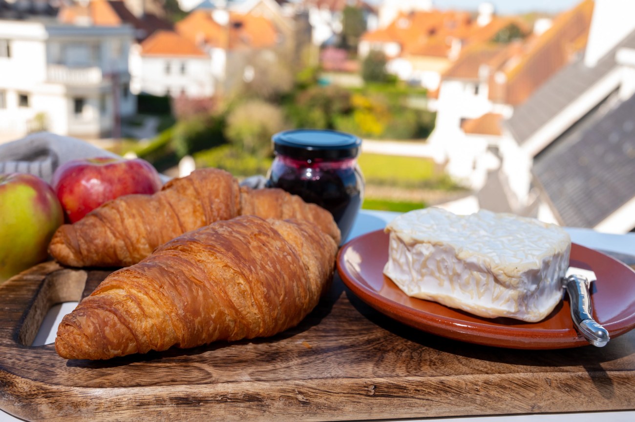 Petit-déjeuner français composé de croissants frais et de fromages de Normandie, de camembert et de neufchâtel, servi en plein air avec une belle vue sur le village français