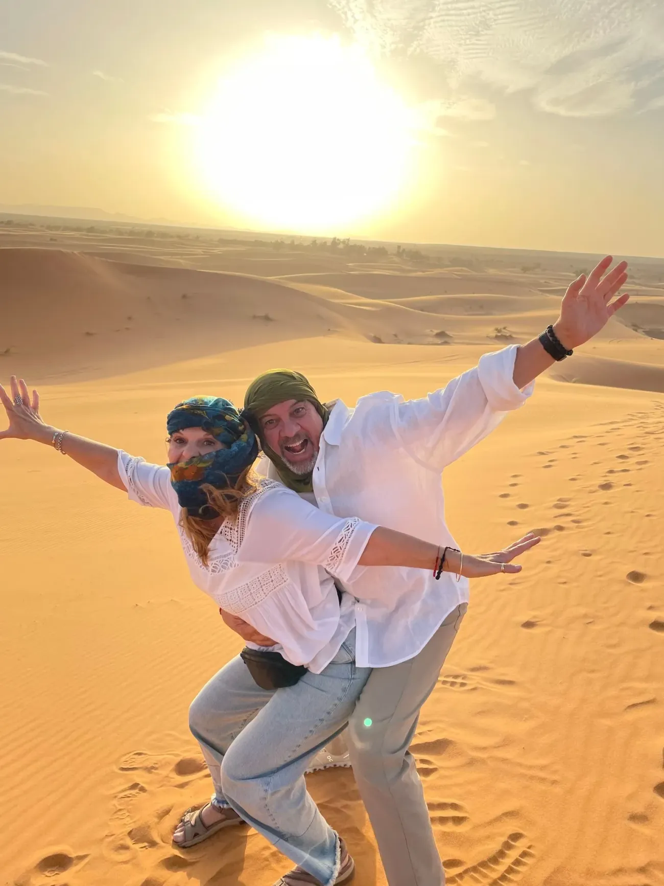 Dunes de sable ensoleillées avec deux voyageurs posant et riant lors d'une visite dans le désert.
