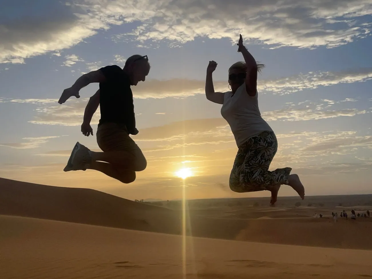 Deux personnes se profilent à mi-saut contre un coucher de soleil sur les dunes de sable du désert du Sahara, au Maroc.