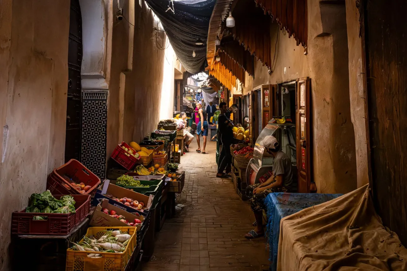 Allée étroite du marché de la médina bordée d'étals de fruits et légumes et d'acheteurs dans la médina, Marrakech, Maroc.