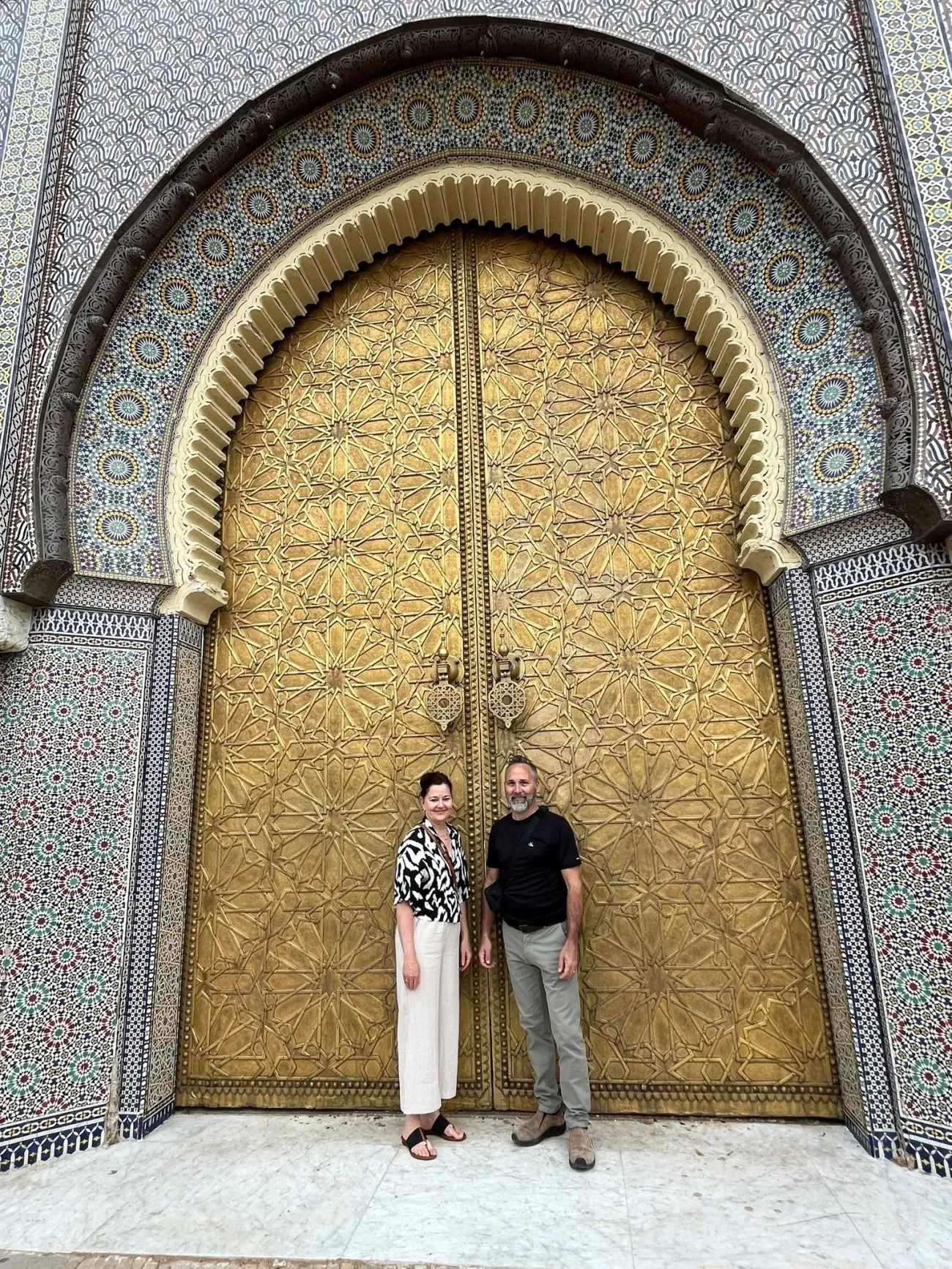 Portes dorées du Palais Royal (Dar el-Makhzen) à Fès, Maroc avec deux voyageurs debout sous l'arche carrelée