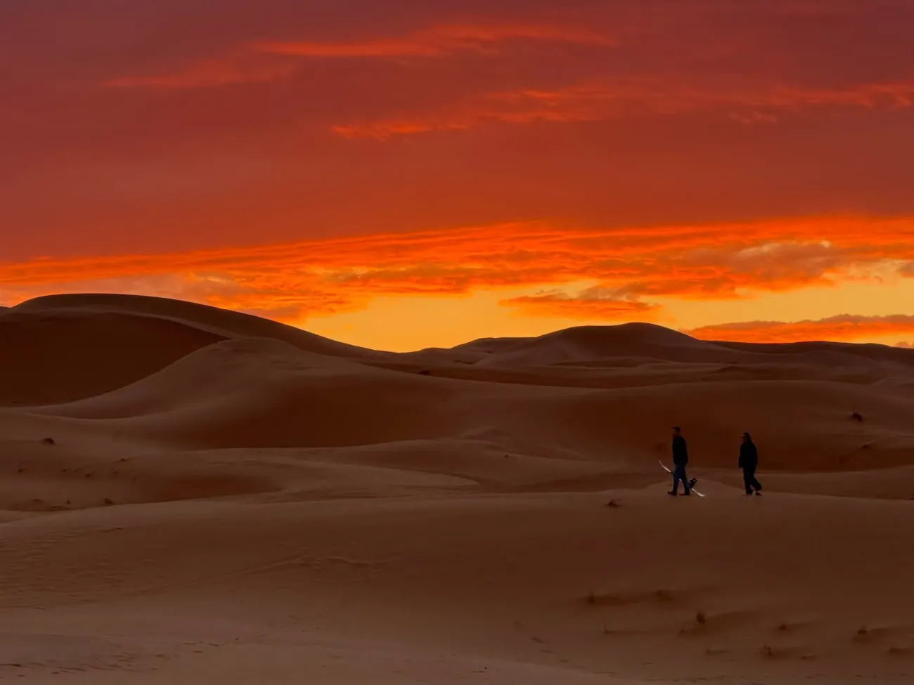 Dunes du désert du Sahara au lever du soleil près d'Erfoud, Maroc, deux personnes marchant sur le sable transportant des planches à sable.