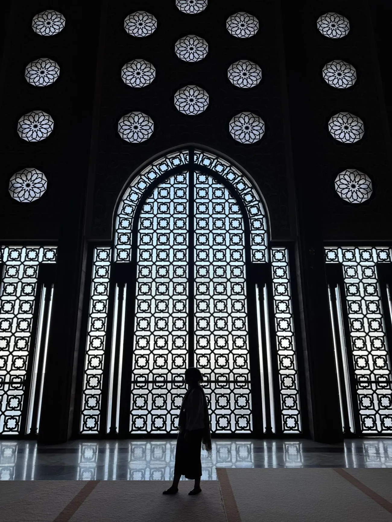 Mosquée Hassan II grande fenêtre cintrée à motifs et écrans sculptés avec une personne silhouettée marchant à l'intérieur, Casablanca, Maroc.