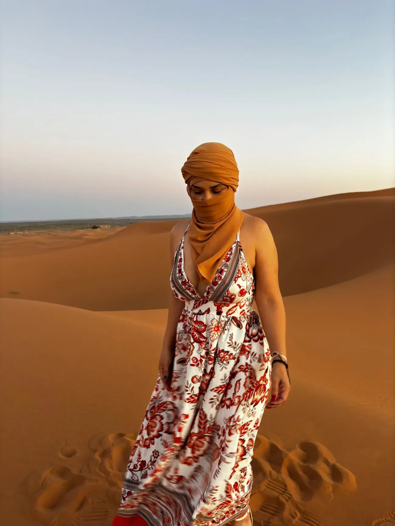 Dunes du désert du Sahara avec une personne portant un bandeau orange et une robe à motifs marchant sur le sable.