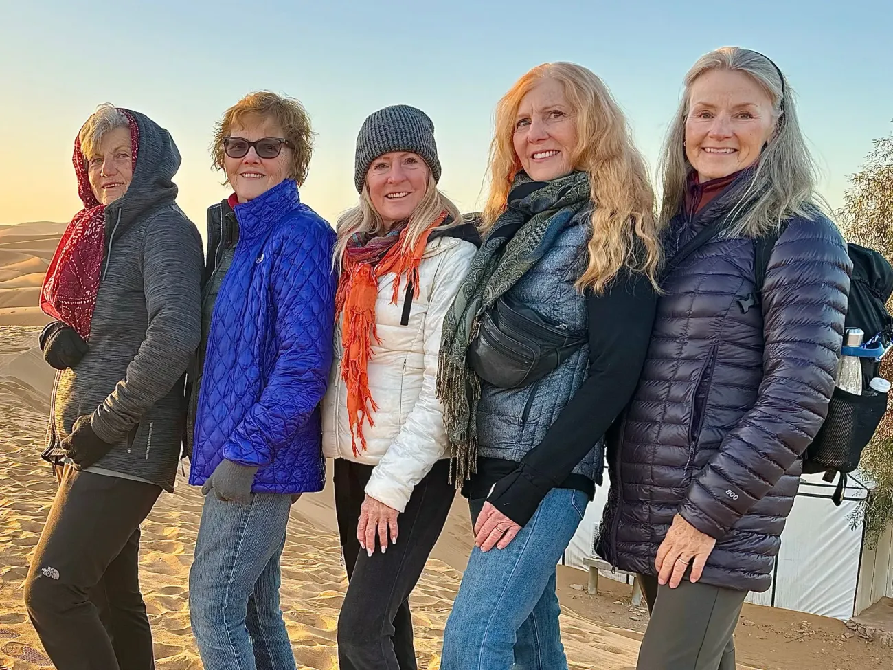 Cinq femmes posant ensemble sur des dunes de sable dans un camp dans le désert du Sahara.