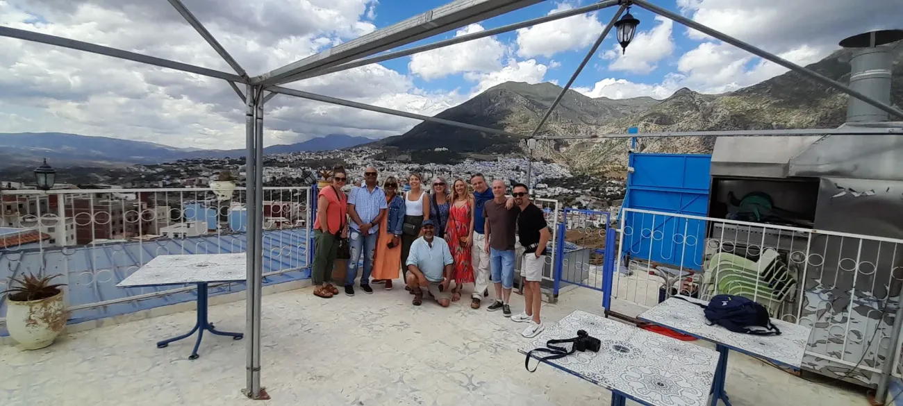 Les toits bleus de Chefchaouen et les montagnes du Rif avec un groupe de voyageurs posant sur un toit-terrasse, Chefchaouen, Maroc.