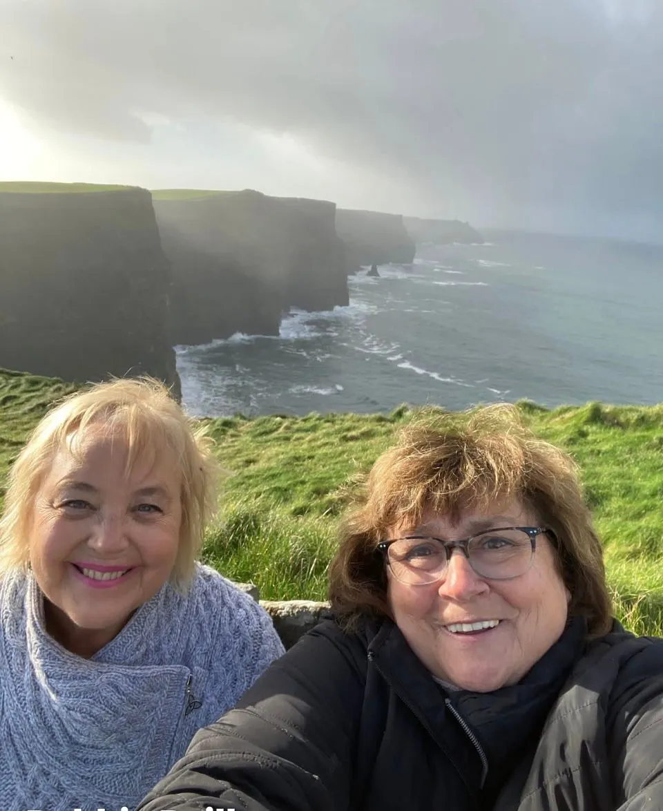 Falaises de Moher et côte atlantique avec deux femmes prenant un selfie au bord d'une falaise herbeuse, comté de Clare, Irlande.