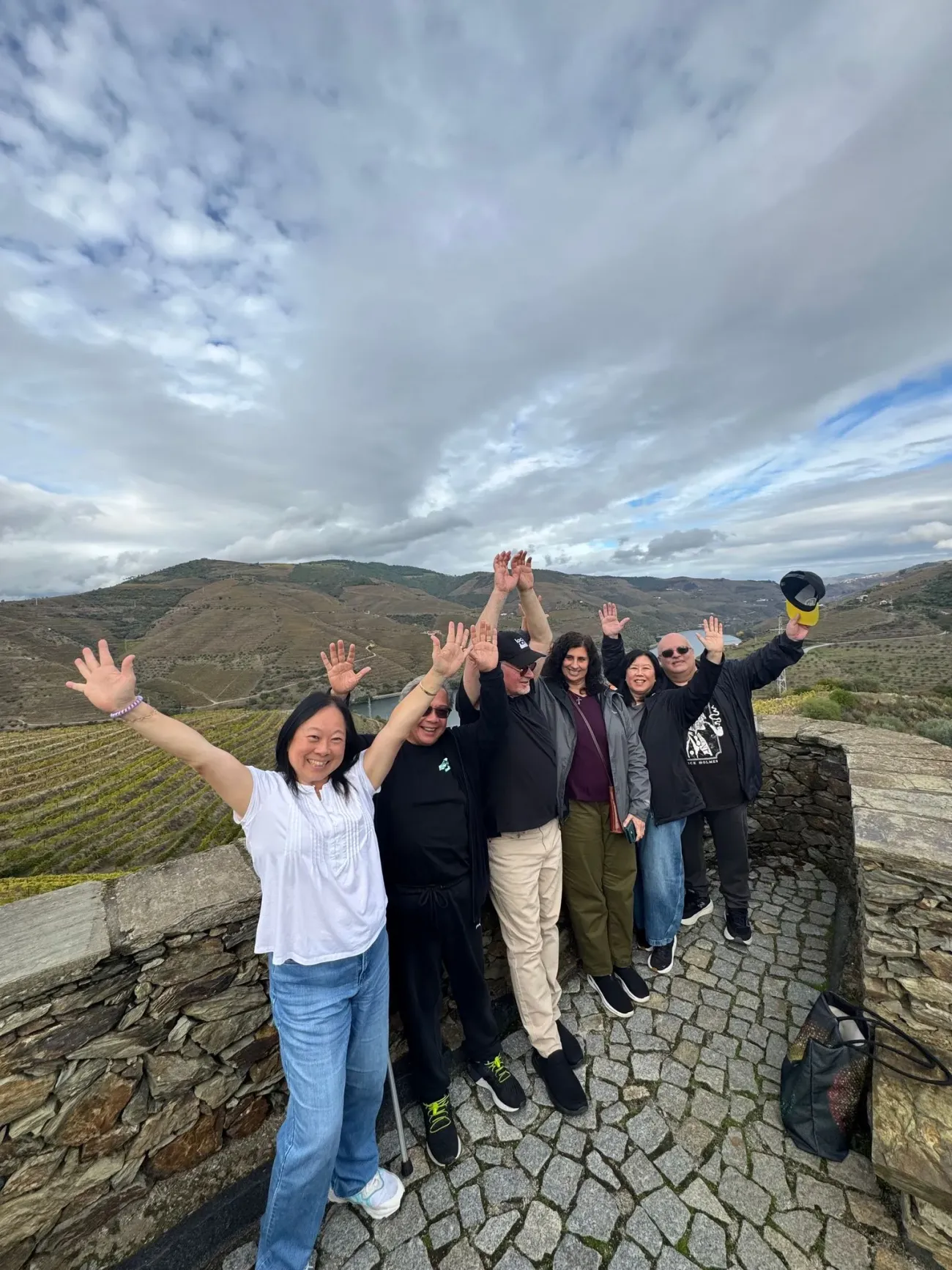 Vignobles en terrasses dans la vallée du Douro avec un groupe d'amis levant la main sur un point de vue en pierre, Portugal.