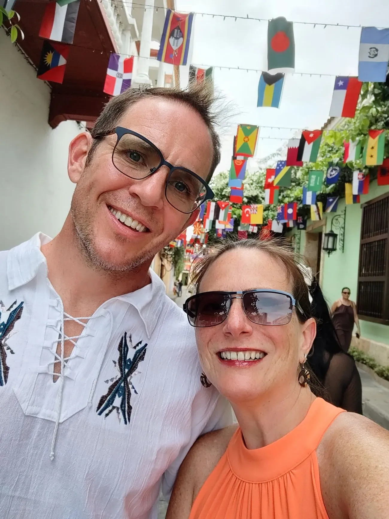 Couple souriant prenant un selfie sous des drapeaux internationaux suspendus dans la vieille ville de Cartagena, en Colombie.