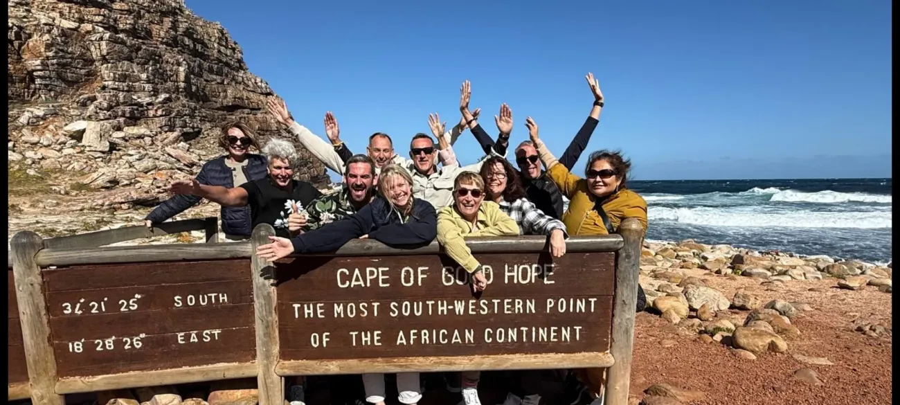Panneau du Cap de Bonne-Espérance avec un groupe de voyageurs s'appuyant dessus et applaudissant près de la côte rocheuse d'Afrique du Sud.